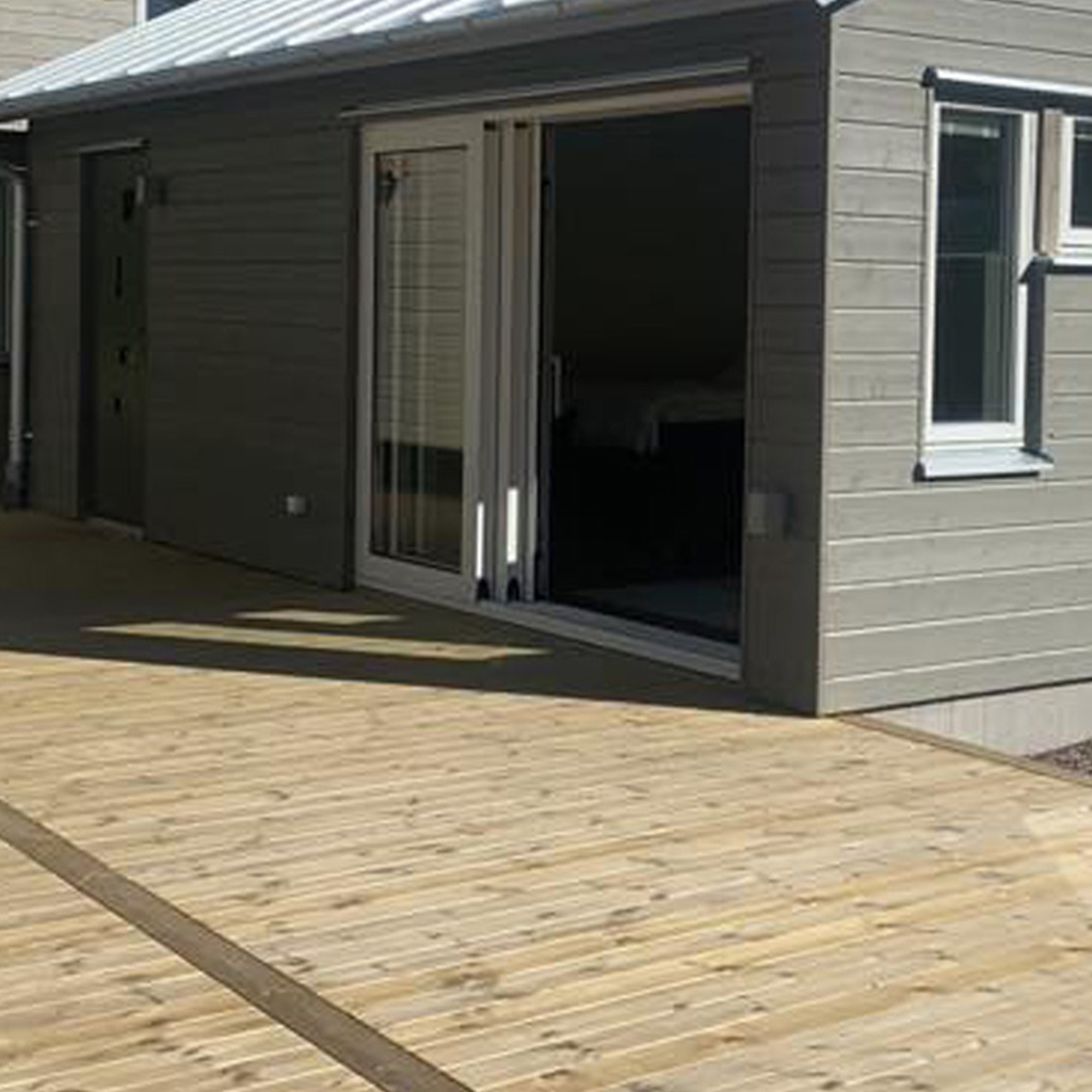sa11 Liten modern byggnad med liggande träpanel, skjutdörr i glas och ny altan i trallvirke.