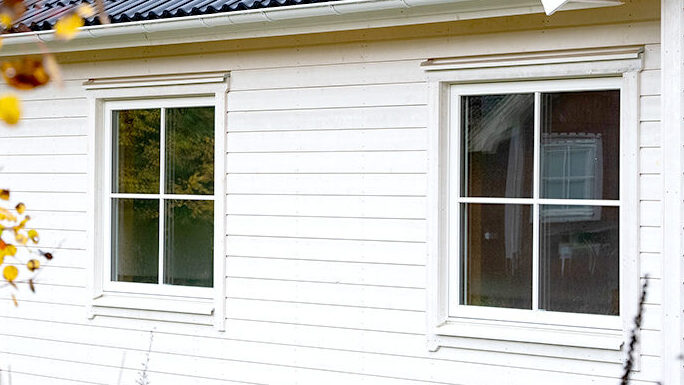fonster Närbild på vit träfasad med två spröjsade fönster på ett bostadshus.