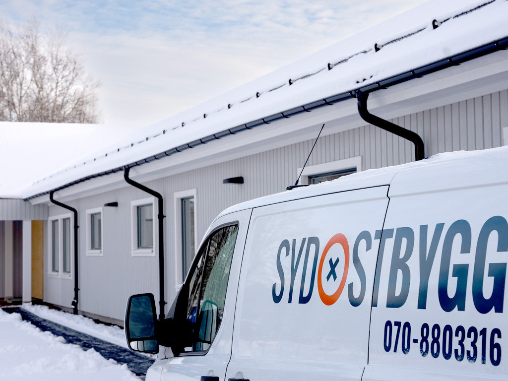 referenscase_vardcentralen Sydostbyggs servicebil parkerad framför nybyggda radhus med snötäckta tak och vita träfasader.